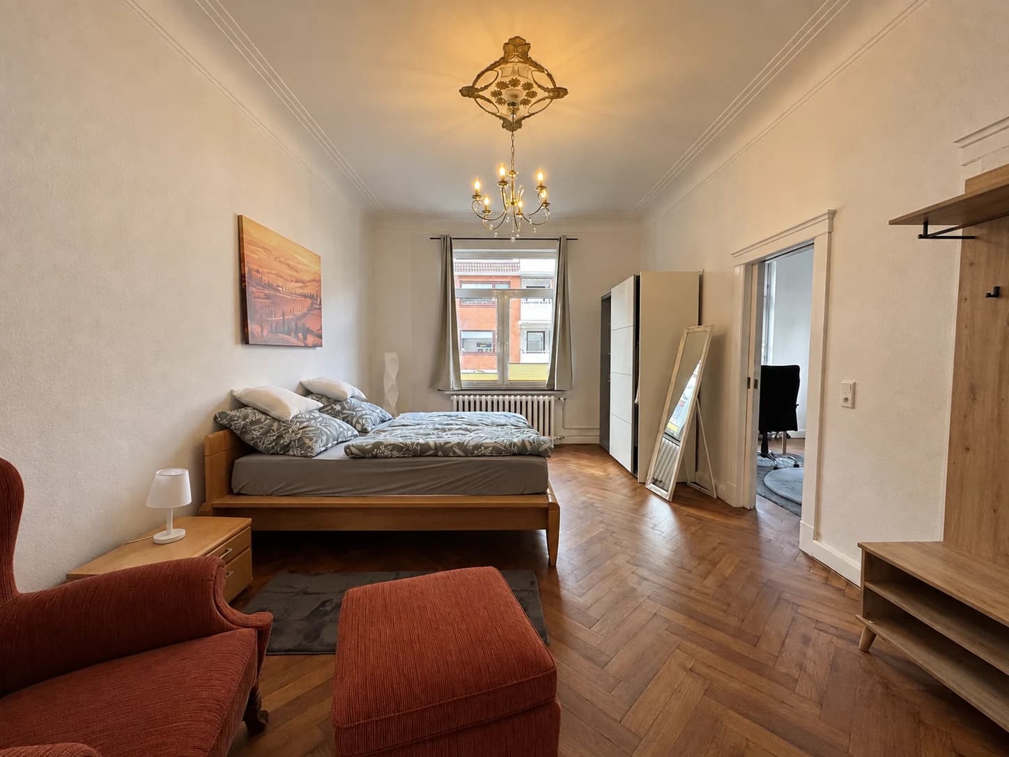 Schlafzimmer mit Doppelbett, Kleiderschrank, Sessel und Holzboden.