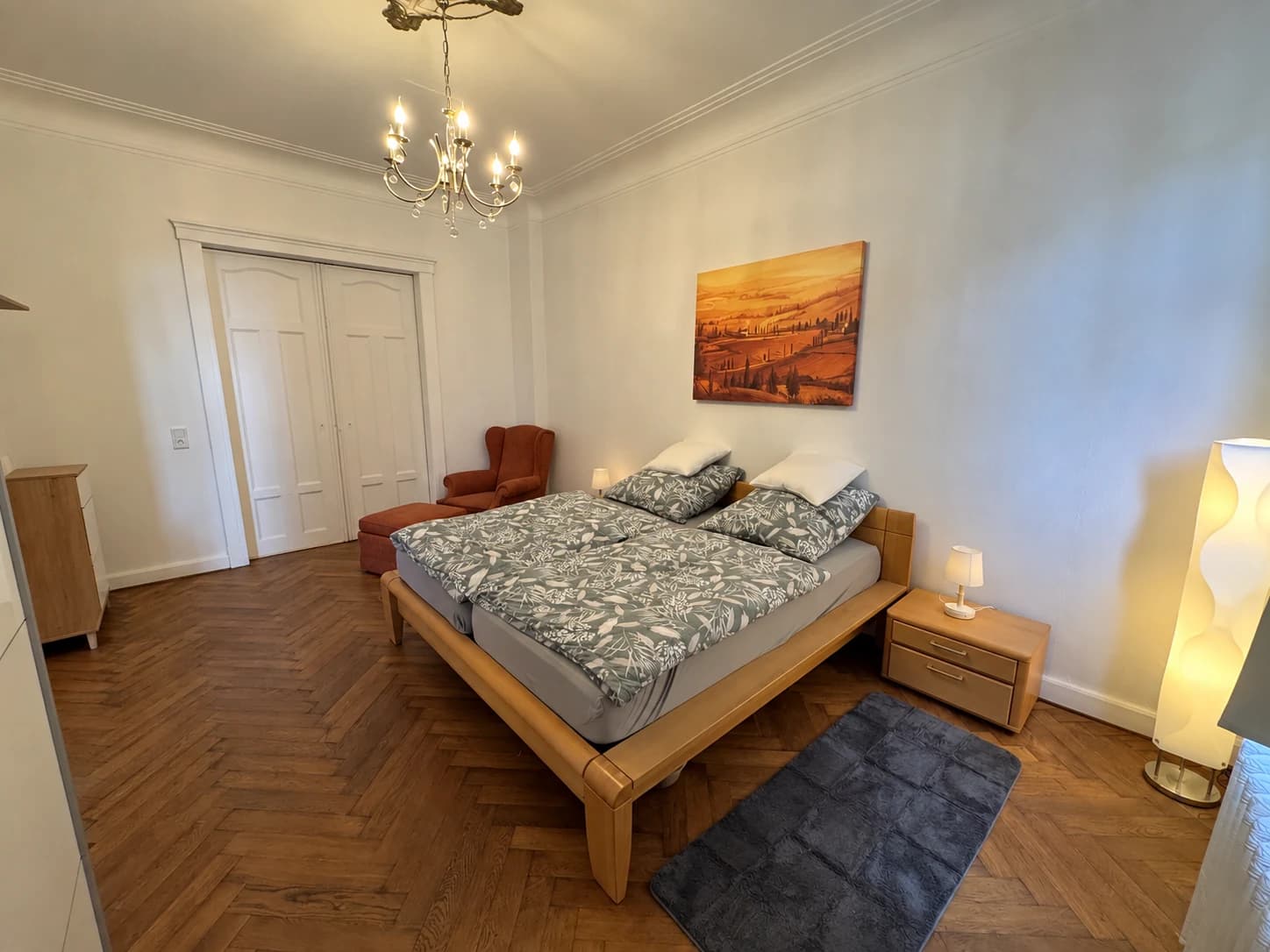 Doppelbett mit Nachttischen, Sessel und Landschaftsbild im Schlafzimmer.
