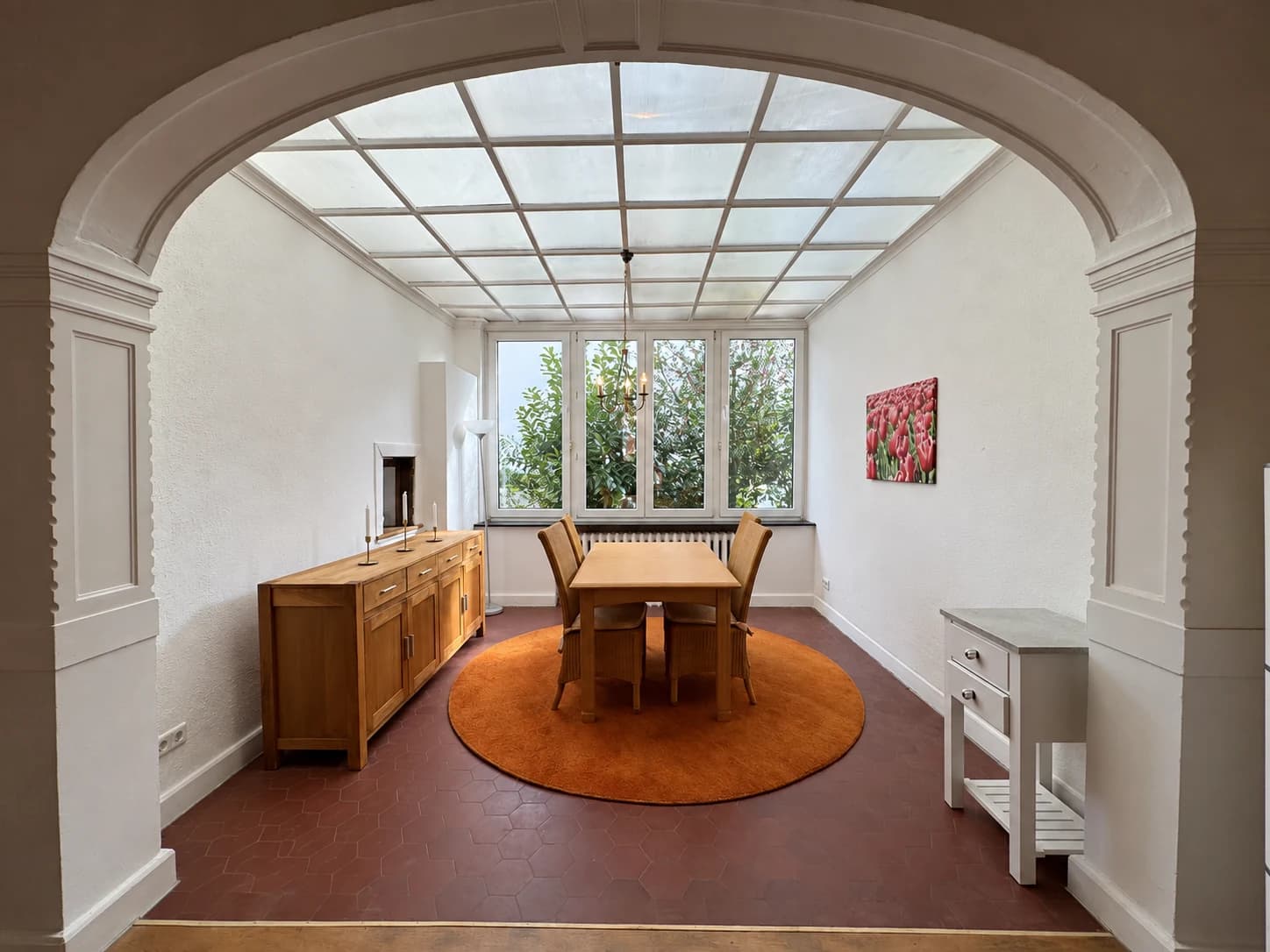 Wintergarten mit Esstisch, Stühlen, Sideboard und großer Fensterfront.
