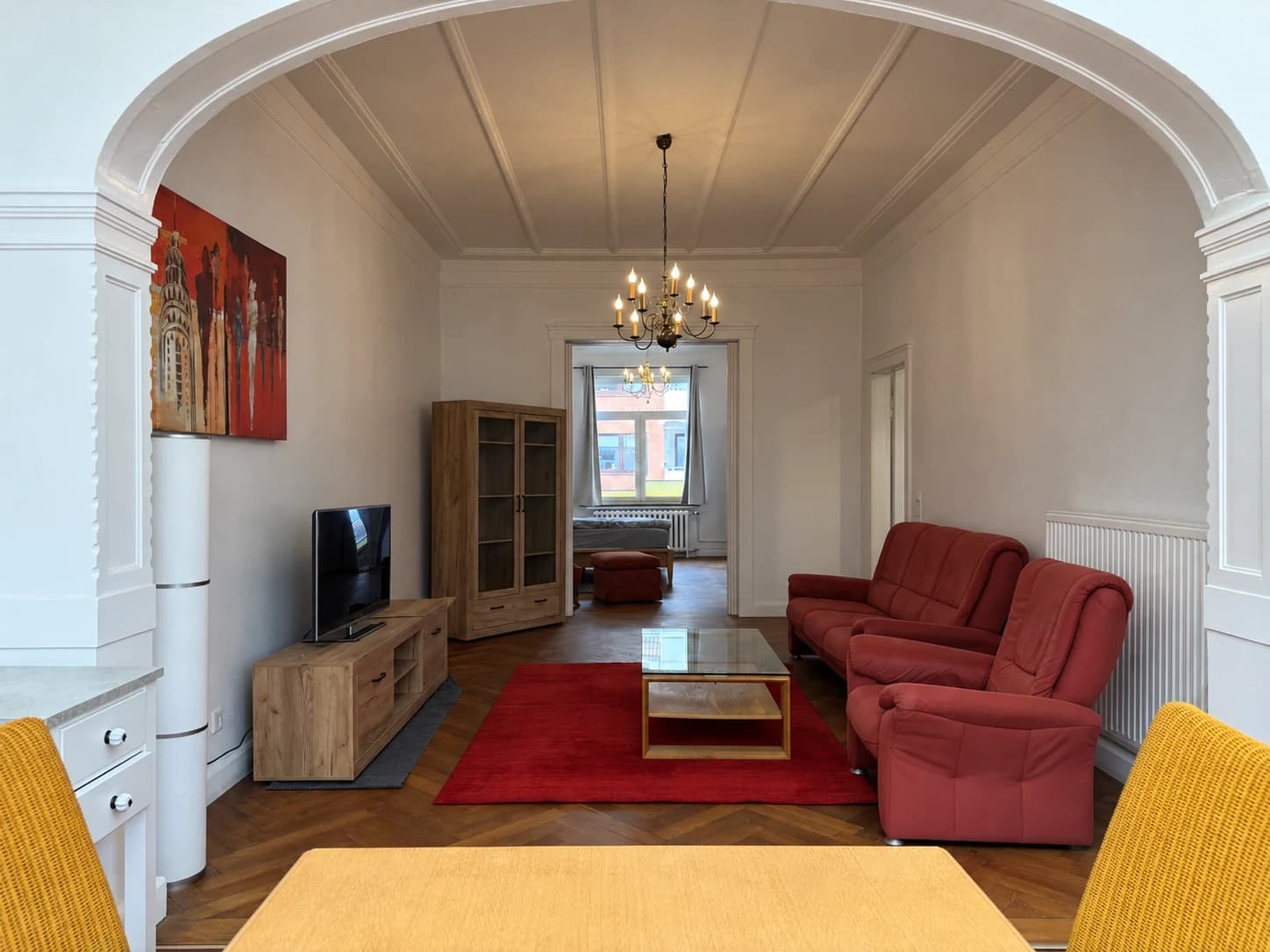 Blick vom Wintergarten ins Wohnzimmer mit rotem Sofa und Holzmöbeln.